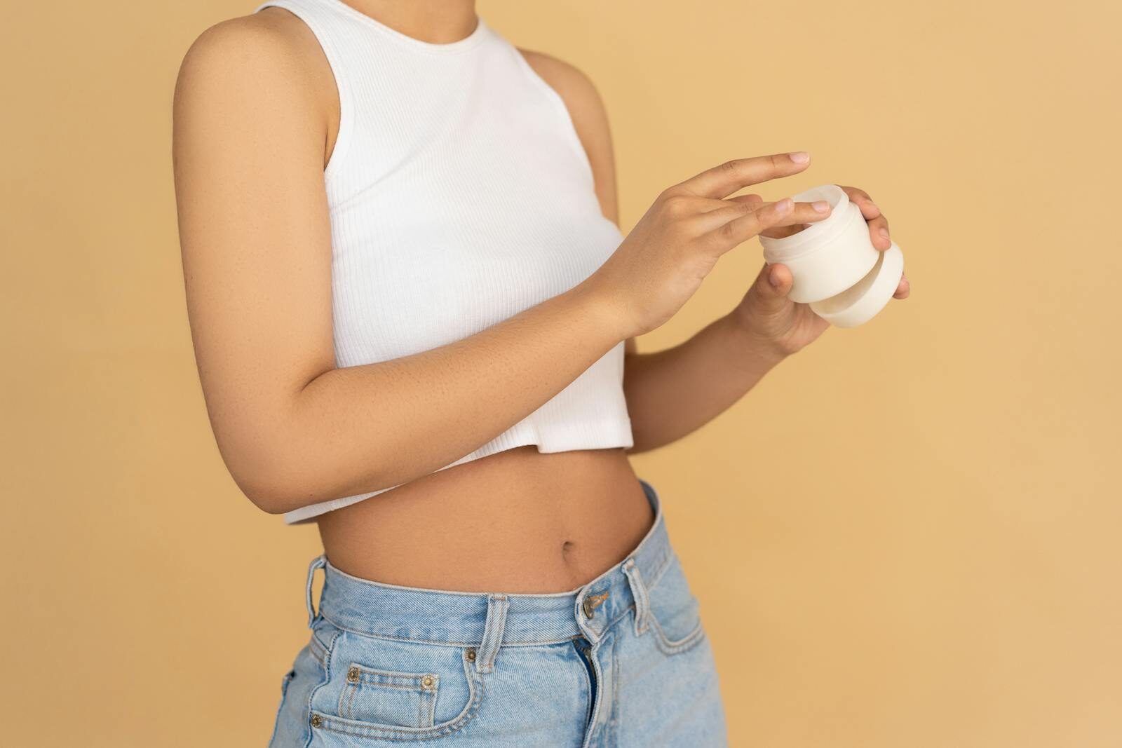 Faceless slim anonymous blond female in sports bra and black leggings in wearable bracelet showing perfect belly on white background while standing with hands on waist