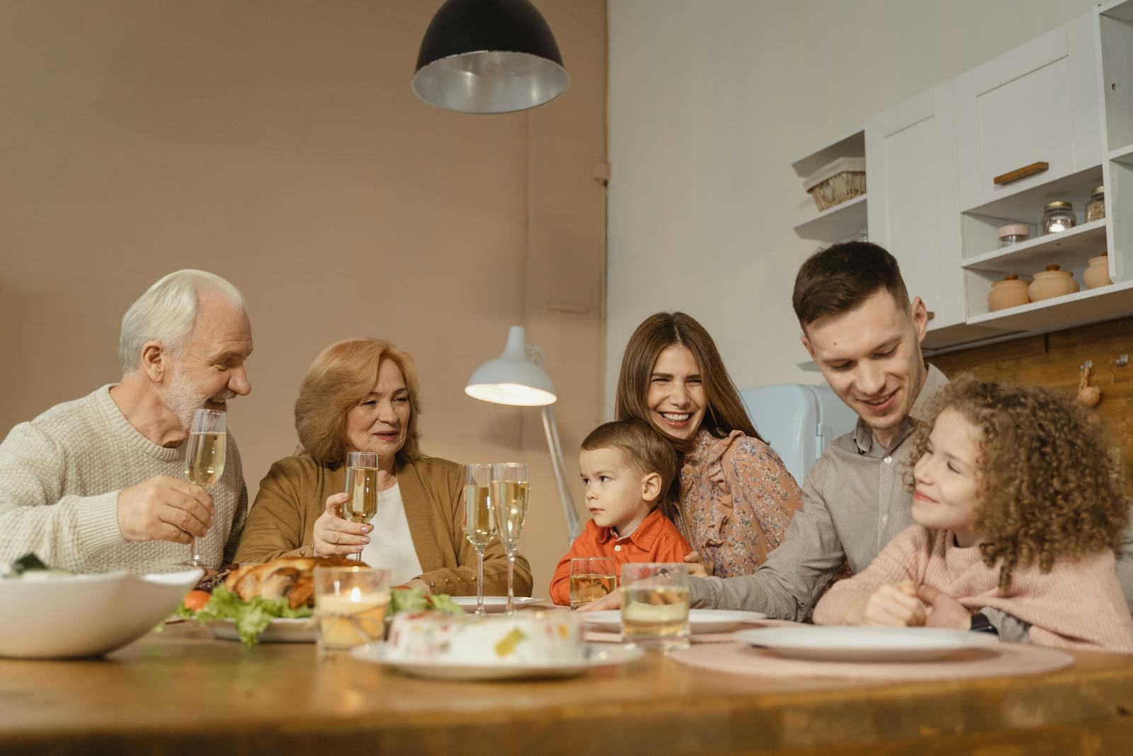 Smiling family of multiple generations enjoying a meal together indoors, sharing laughter and drinks.