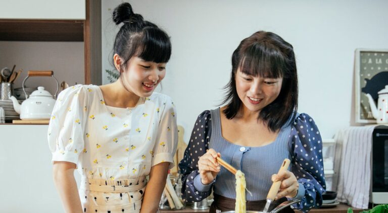 Happy mother and daughter preparing a noodle dish in a modern kitchen.