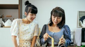 cheerful asian women boiling noodles in kitchen